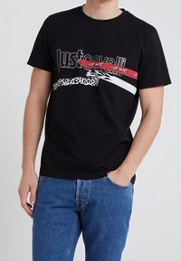 Camiseta de algodón negra con un vibrante texto gráfico en rojo y blanco y acentos de estampado de leopardo. Mangas cortas y escote redondo.