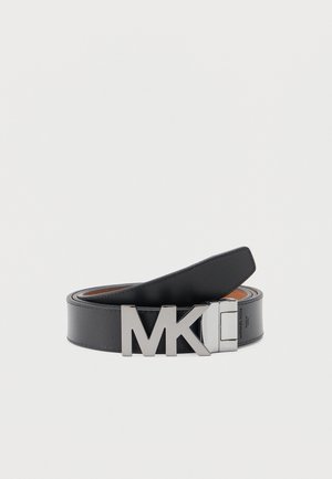 Cintura in pelle nera arrotolata con grande fibbia metallica argentata "MK" su uno sfondo chiaro e uniforme.