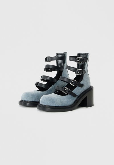 Blue suede ankle boots with black leather straps, buckle details, wide block heels, and a rounded toe design.