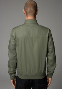 Olijfgroene bomberjack met een gladde, matte afwerking, ribgebreide manchetten en kraag, en een naaddetail over de bovenrug.