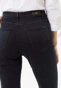 Tummansiniset farkut slim fit -mallilla, joissa on BRAX-brändin vyötärö, kaksi takataskua ja hienovaraisesti teksturoitu kangas.