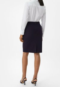 Marineblaue Bleistiftrock mit Rückenschlitz, kombiniert mit einem weißen, langärmligen Hemd mit Knöpfen. Der Rock zeichnet sich durch ein figurbetontes Design und eine glatte Textur aus.