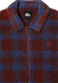 Fleece zip-up jakke i brun og blå plaid. Har en krave, en frontlynlås og et lille logo på brystet. Blødt, struktureret materiale.