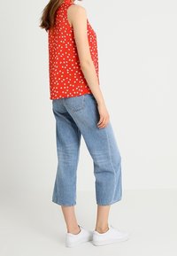 Röd ärmlös topp med vitt blommönster, i kombination med ljusblå cropped jeans och vita sneakers, som visar upp en avslappnad outfit.