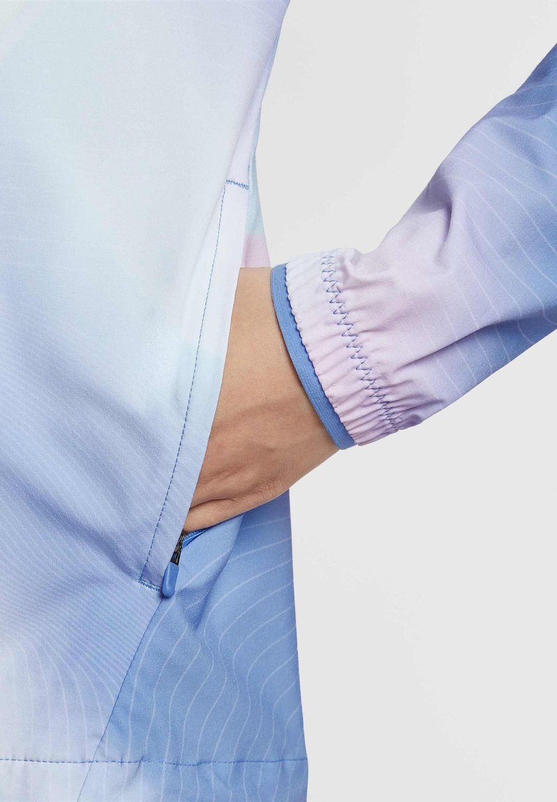 Lichtgewicht jack met een gradient ontwerp in lichtblauw en lavendel, met elastische manchetten en een ritszak aan de zijkant. Zachte textuur.