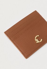 Καφέ δερμάτινη θήκη καρτών με τρεις υποδοχές και μικρό χρυσό διακοσμητικό κούμπωμα σε λευκό φόντο.