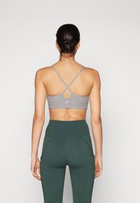 Grå sportsbh med en nøkkelhull-detalj og kryssede stropper, kombinert med høyt liv grønne leggings. Glatt stoff, minimal design.