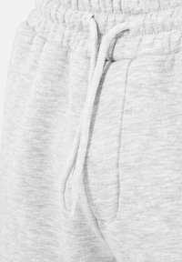 Close-up van lichtgrijze joggingbroek met elastische tailleband, aantrekkoorden en voorzak met zachte stoftextuur.