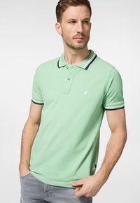 Miętowa koszulka polo z mieszanki bawełny, z kontrastowym czarno-białym kołnierzykiem i mankietami oraz małym logo na piersi.