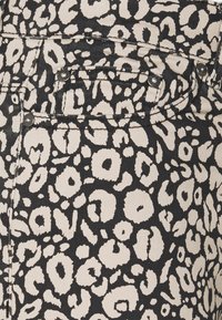 Tessuto leopardato con sfondo nero e macchie beige. Materiale denim presenta accessori in argento e dettagli di cucitura a contrasto.