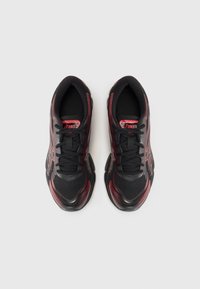 Sapatos atléticos pretos com detalhes em vermelho, parte superior em malha, bico redondo e cordões planos. Apresenta a marca Asics na língua e nos painéis laterais.