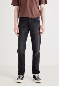 Dark denim jeans with a slim fit, featuring five pockets and subtle fading. Paired with black and white canvas sneakers and a brown shirt.