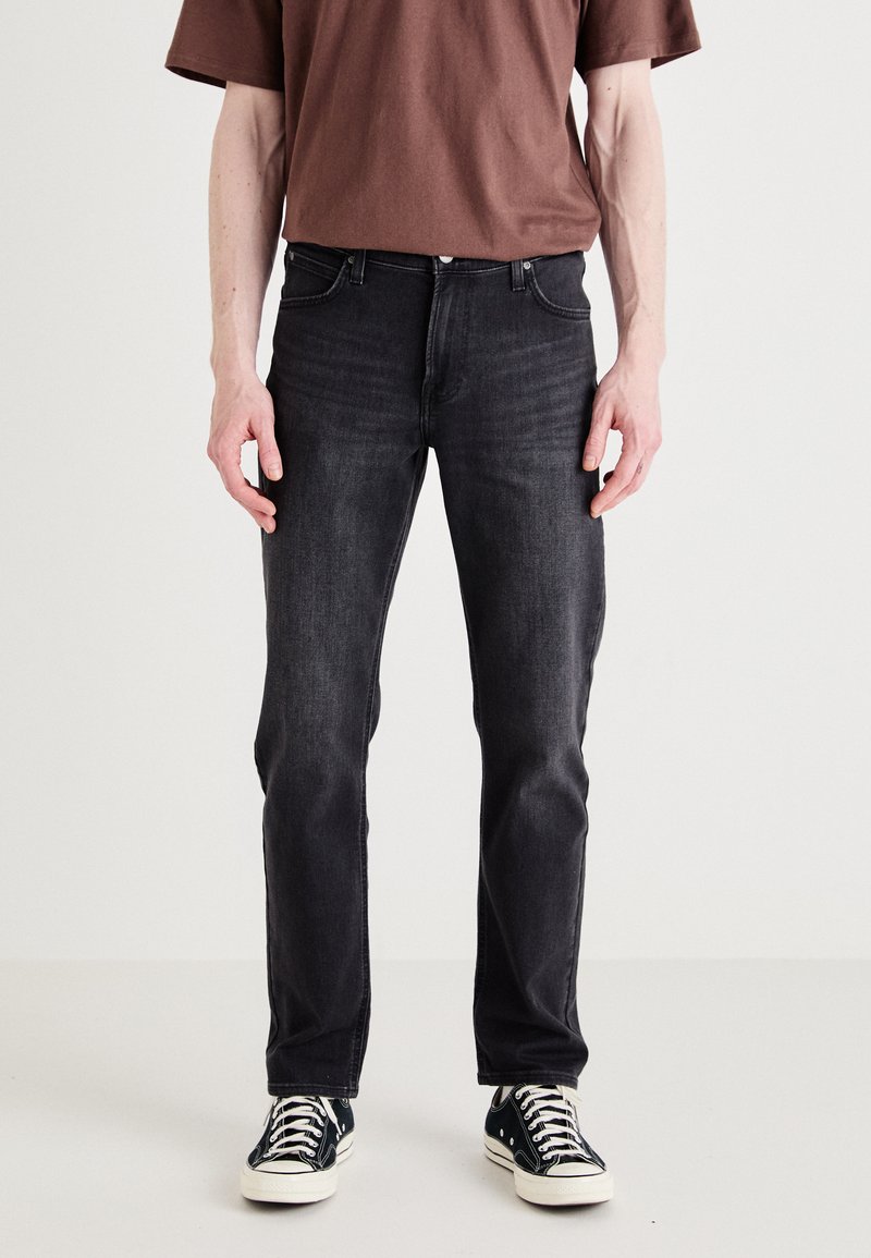 Dark denim jeans with a slim fit, featuring five pockets and subtle fading. Paired with black and white canvas sneakers and a brown shirt.