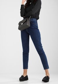 Jeans blu a vita alta con vestibilità slim, abbinati a una blusa a righe nere e bianche e mocassini neri, completati da una borsa nera.