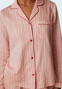 Rosa randig pyjamasöverdel med röda och vita vertikala ränder, krage, bröstficka och röda knappar längs fram. Mjuk bomullsmaterial.
