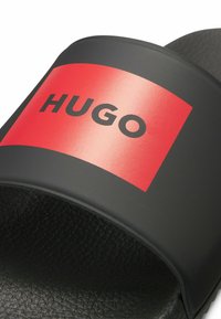 Infradito neri con una fascia testurizzata e un ampio design rettangolare rosso. Il design include la parola "HUGO" in grassetto nero.