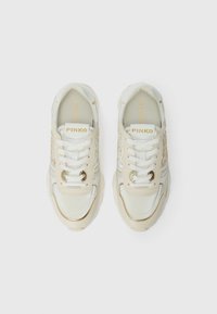 Un paio di scarpe da ginnastica beige e bianche con lacci, dettagli dorati e branding "PINKO" sulla linguetta e sulla soletta, viste dall'alto.