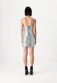 Silver sequined mini dress with thin straps, fitted silhouette, and a geometric pattern. Worn with black heeled shoes and ankle socks.