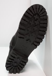 Suela de goma negra de una bota que presenta surcos profundos y patrones cruzados, con el nombre de la marca "NEW LOOK" grabado en la base.