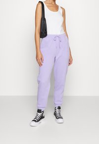 Light purple sweatpants with an elastic waistband and drawstring detail. Styled with a white tank top and black high-top sneakers.