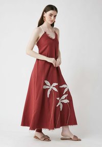 Rotes Maxikleid mit Spaghettiträgern, das eine fransige Ausschnittkante und weiße, gestickte Blattmuster am Saum aufweist. Glatte Stofftextur.