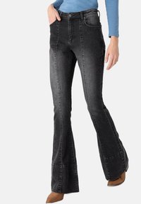 Black flared jeans made of denim, featuring a high waist, front pockets, and contrasting stitching details. The fabric has a worn appearance.