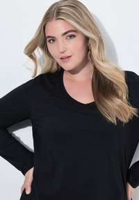 Schwarzes Langarmoberteil aus weichem Stoff mit V-Ausschnitt. Es hat eine lockere Passform und betont die Konturen mit einer glatten Textur.