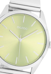 Montre en argent avec un boîtier rond, dotée d'un cadran soleillé vert clair et d'index horaires en argent. Mécanisme à quartz avec un bracelet en métal.