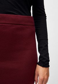 Burgundy stickad kjol med ribbad midja, i kombination med en åtsittande svart långärmad topp. Tyget har ett texturerat, mjukt utseende.