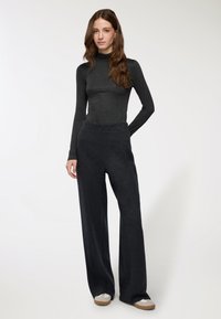 Maglione dolcevita aderente grigio scuro abbinato a pantaloni larghi e comodi grigio scuro. L'outfit presenta una texture morbida e una cintura elastica.