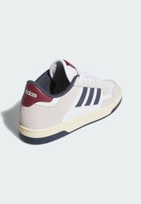 White and beige sneaker with navy accents, suede and leather materials, featuring three navy stripes and a maroon heel cap. Rubber outsole.