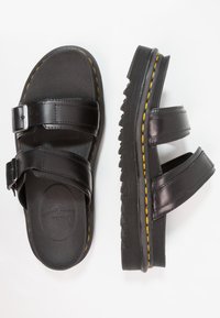 Sandali neri con due cinturini regolabili, realizzati in pelle liscia; suola testurizzata con cuciture gialle e un design spesso e scanalato.