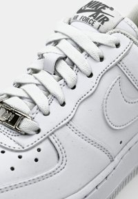 Närbild av vita Nike Air Force 1-sneakers som visar snörning, varumärket på tungan och den sömda Nike-swooshen på sidan.