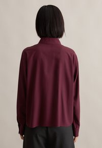 Burgundy long-sleeve shirt with a relaxed fit, featuring a collared neckline and buttoned cuffs, made of smooth fabric with a matte finish.