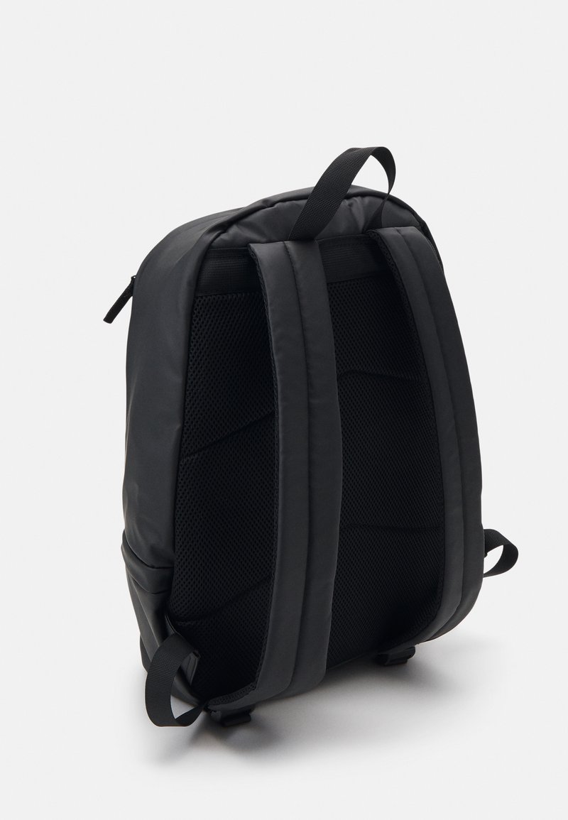 Mochila negra con respaldo acolchado de malla y correas ajustables. Presenta una textura suave y mate, así como un diseño rectangular y elegante.