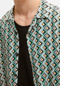 Chemise à manches courtes avec un motif géométrique multicolore composé de triangles sur un fond blanc, complétée par un T-shirt noir en dessous.