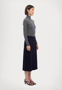 Gray fitted turtleneck sweater, knee-length navy skirt with a side detail, and black strappy heeled sandals. Textured knit fabric.