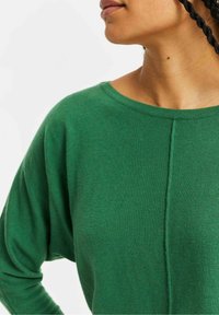 Grön stickad tröja med rund halsringning, sänkta axlar och en mittsöm. Mjuk textur, lättviktig och avslappnad design.