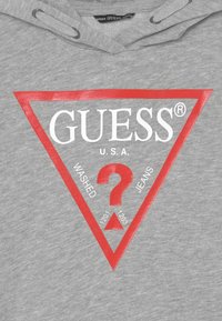 Felpa grigia con cappuccio caratterizzata da un grande logo triangolare rosso con la scritta "GUESS® U.S.A." e "WASHED JEANS", insieme a un punto interrogativo centrale.