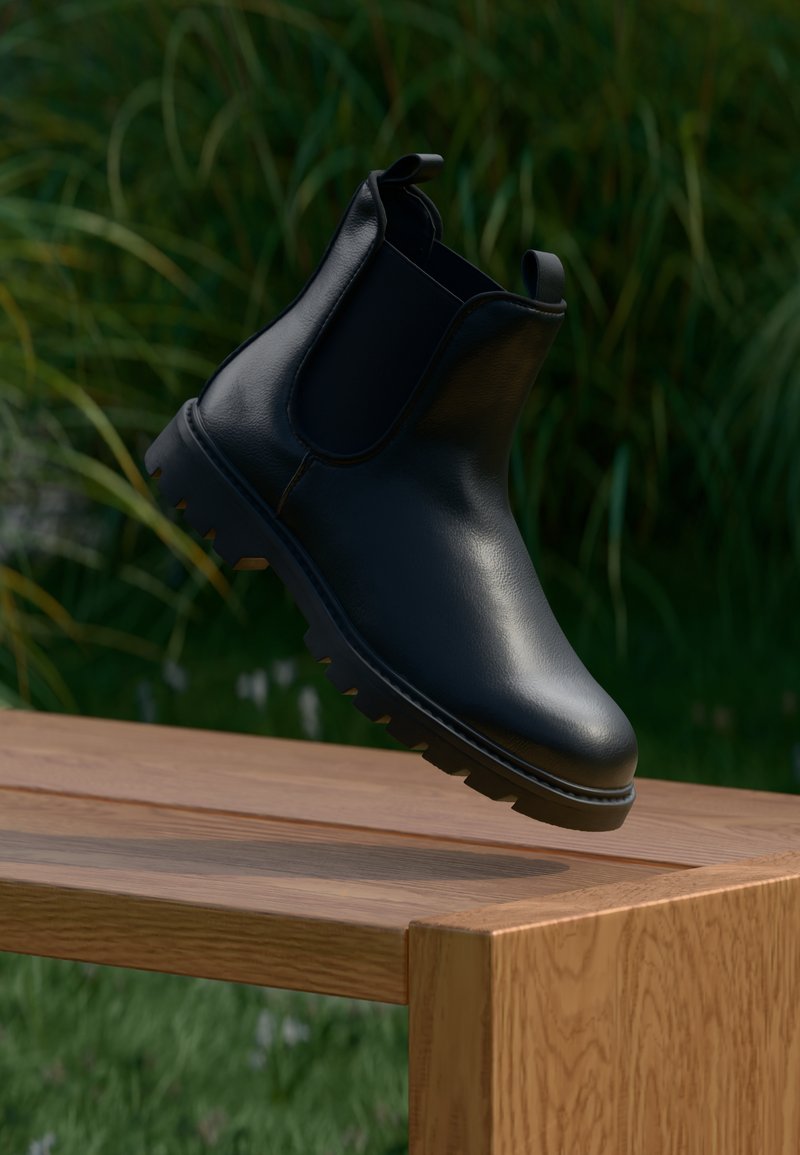 Bota Chelsea de cuero negro con punta redonda, paneles laterales elásticos, tiradores y suela de goma texturizada, colocada sobre una superficie de madera.