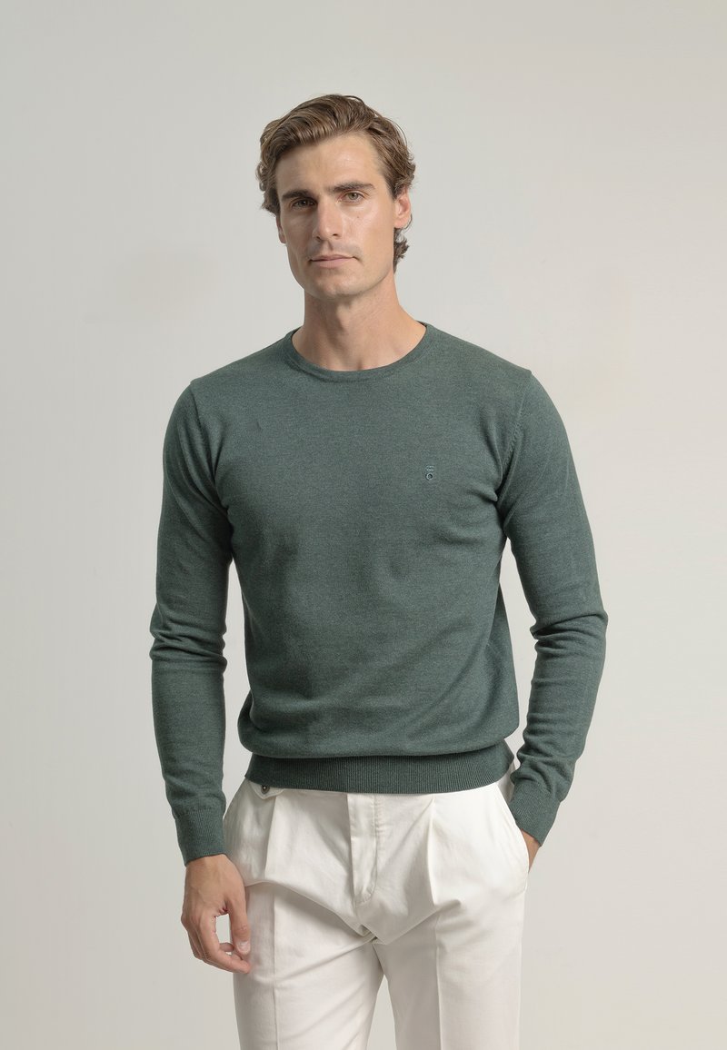Suéter verde oscuro de tela de punto suave con cuello redondo y mangas largas. Puños y dobladillo acanalados, con un pequeño logo en el pecho.