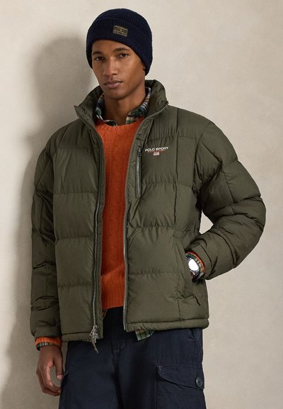 Olivengrøn dunjakke med quiltet tekstur, lynlåslukning og Polo Sport-logo. Båret over en orange sweater og ternet skjorte. Marineblå beanie.