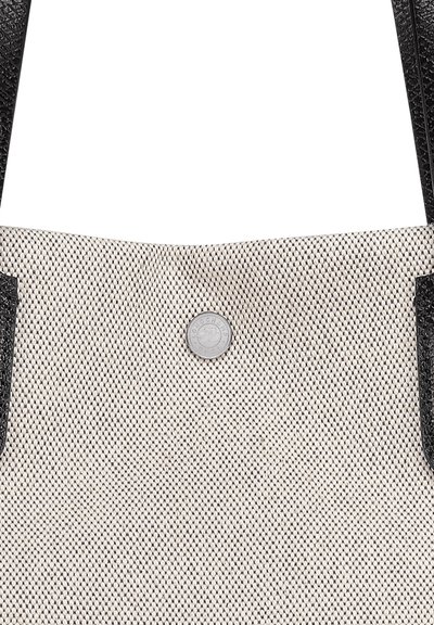 Tote bag featuring a textured cream body with black leather accents and a circular silver snap button closure. Handle straps are also black leather.