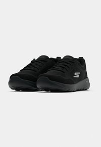 Paire de baskets de sport noires avec empeignes en mesh, fermetures à lacets et logo gris « S » sur les côtés, affichées sur fond blanc.