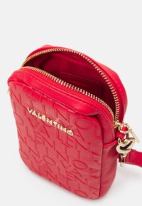 Saco cruzado de couro vermelho com design de logotipo em relevo, zíper dourado e detalhes em metal. Textura suave com uma forma retangular compacta.