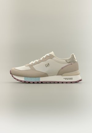 Beige og hvid sneaker med snøredesign, blå accent på sålen, "GAP" logo på siden og tekstureret gummiydersål for greb.