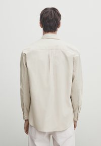 Jasno beżowa koszula z długim rękawem w luźnym kroju, z klasycznym kołnierzykiem i mankietami zapinanymi na guziki, uszyta z gładkiego, lekkiego materiału.