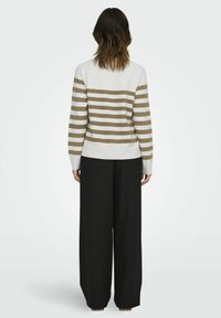 Pull rayé blanc et beige avec un ourlet côtelé, associé à un pantalonlarge noir, vu de dos. Tissu texturé, coupe décontractée.