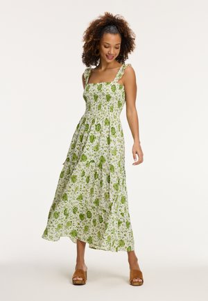 Maxi dress in white with green floral pattern. Features square neckline, ruffled straps, and a textured bodice. Flowy fabric drapes elegantly.