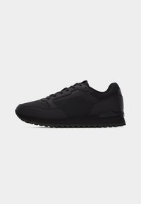 Baskets de sport basses noires avec panneaux texturés, fermeture lacets et semelle en caoutchouc, présentées en profil latéral sur fond uni.